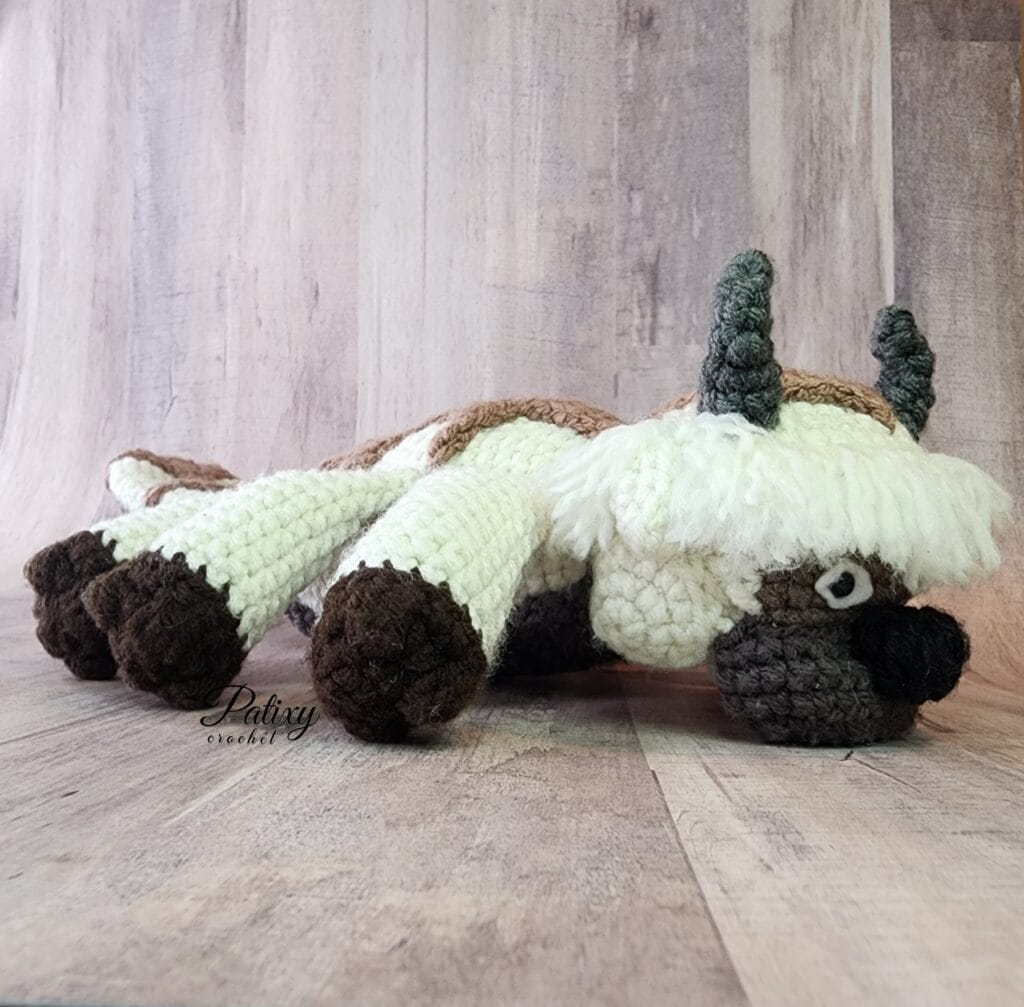 Appa - Esp AMIGURUMI , acostado con las patas extendidas sobre una mesa de madera